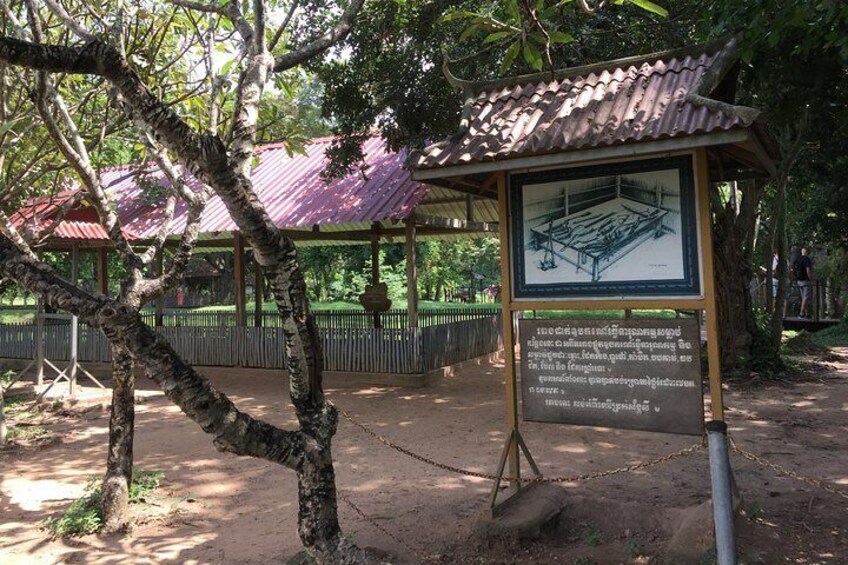 A historical site with a metal roof structure, a signboard with text, and a chain-link fence. 2