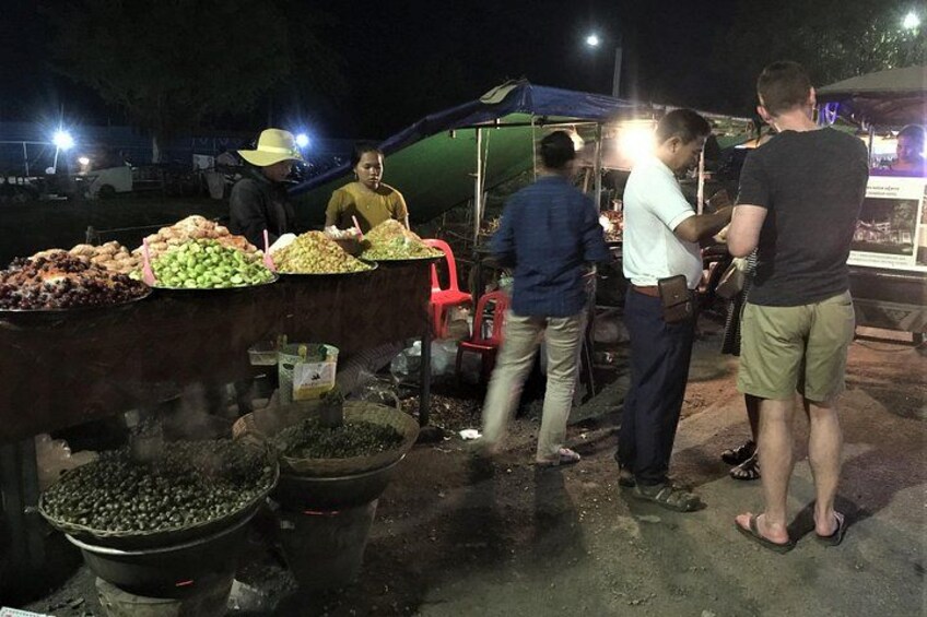 A nighttime outdoor market with people shopping and a vendor selling food. 5