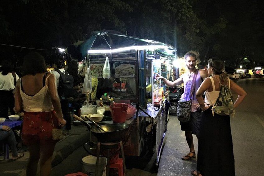 A nighttime street food stall with people gathered around it. 4