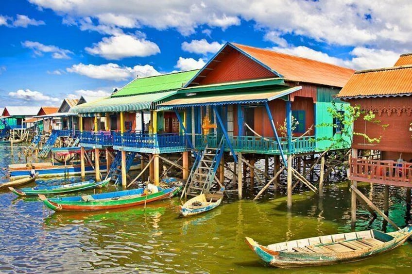 A traditional stilt house with a green roof and blue railings, surrounded by calm water and boats. 2
