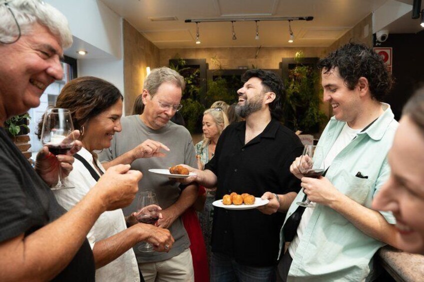 A group of people dining indoors, holding plates and glasses of food and drink. 1