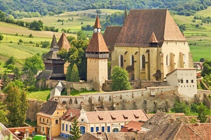 A historic castle with multiple towers, surrounded by a fortified wall and lush green fields. 4