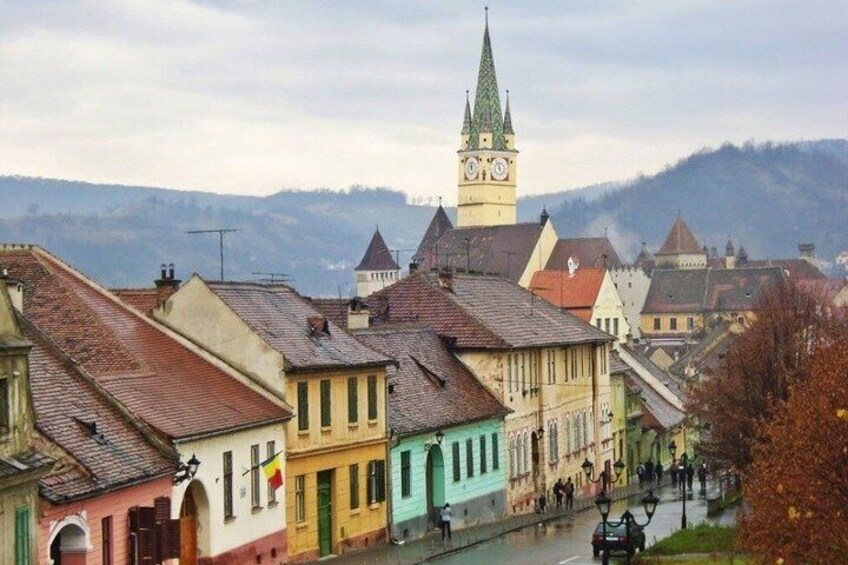 A town with colorful buildings, a prominent clock tower, and a river. 2