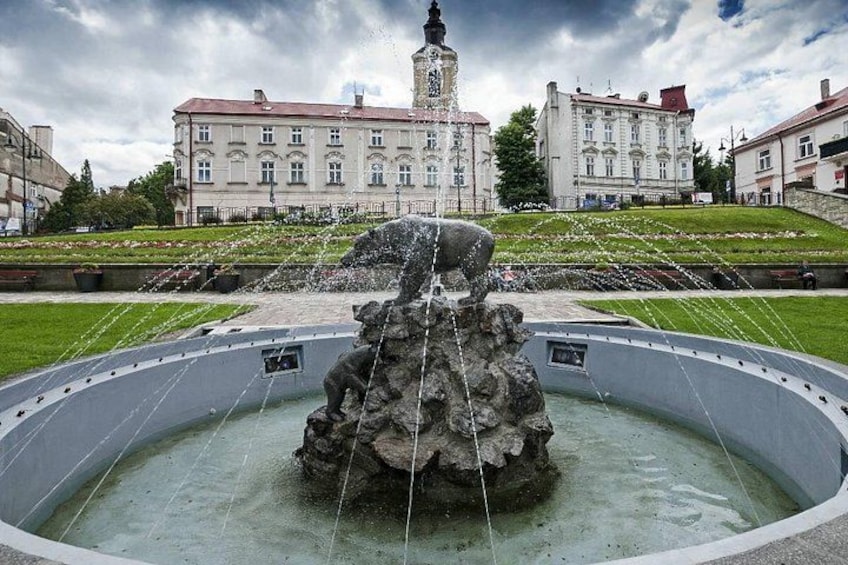 A fountain with water jets in a circular basin, surrounded by a grassy area with a large building in the background. 1