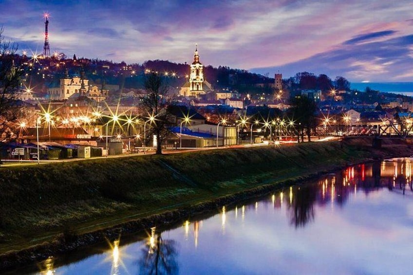 Un paisaje urbano nocturno con edificios iluminados, un río que refleja las luces y una torre destacada a lo lejos. 1