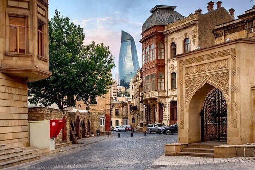 A cobblestone street with historic buildings, a tree, and a modern skyscraper in the background. 1