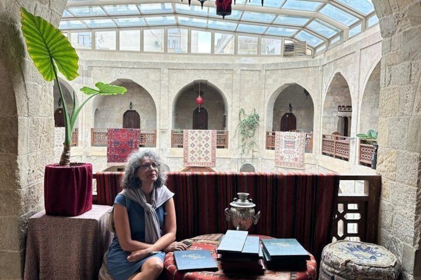A woman sitting at a table with books in a courtyard with arches and a glass ceiling. 3