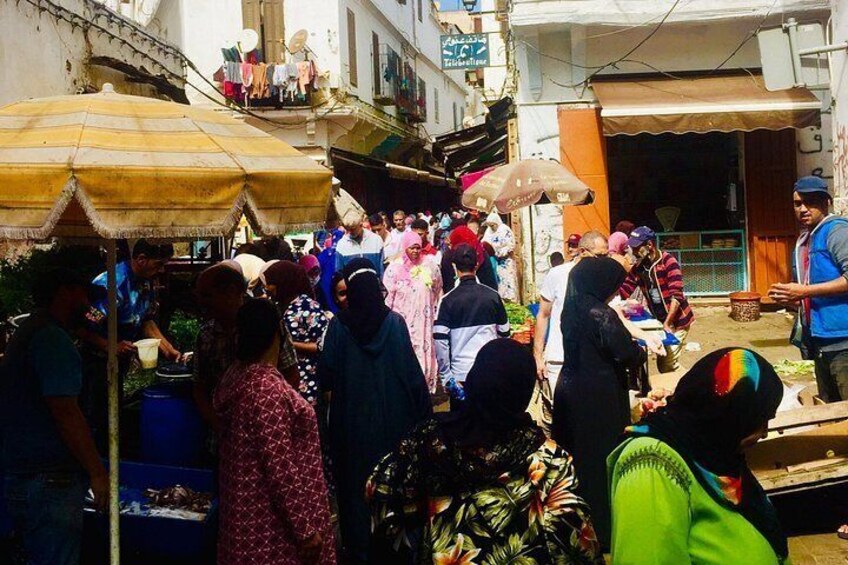 A crowded outdoor market with people shopping and vendors selling goods. 5