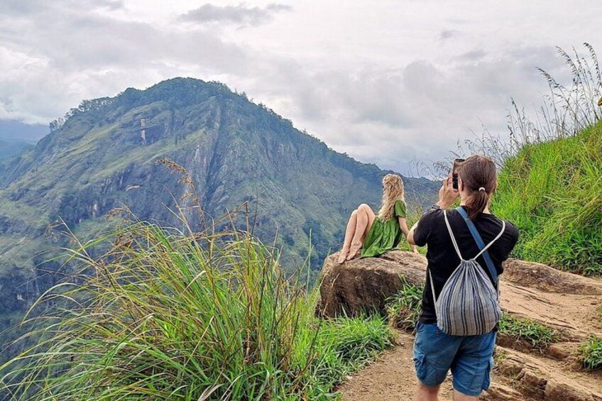 Una persona fotografiando un paisaje montañoso con una mujer sentada sobre una roca. 1
