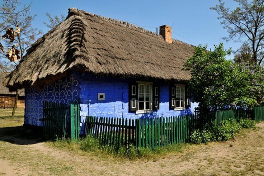 Una casa azul con techo de paja y valla verde. 1
