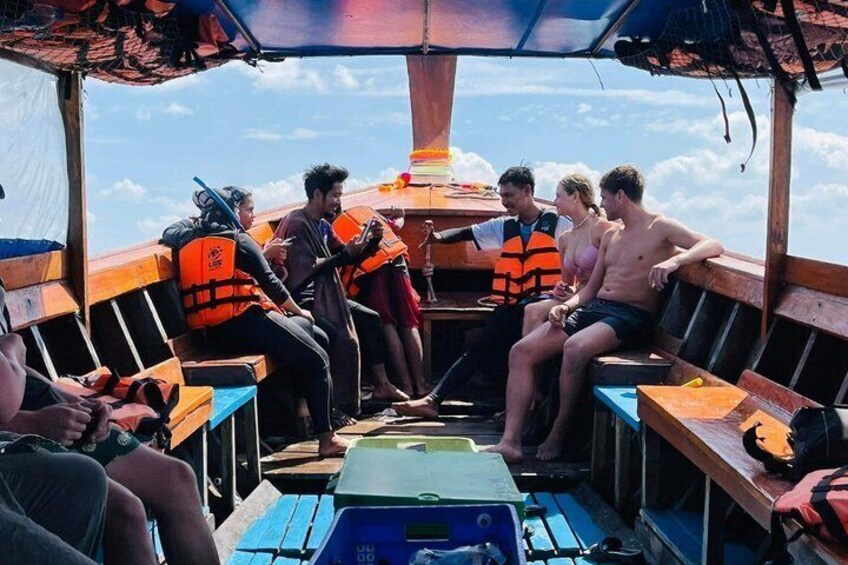 A group of people on a boat with life jackets, wooden benches, and a blue cooler. 4