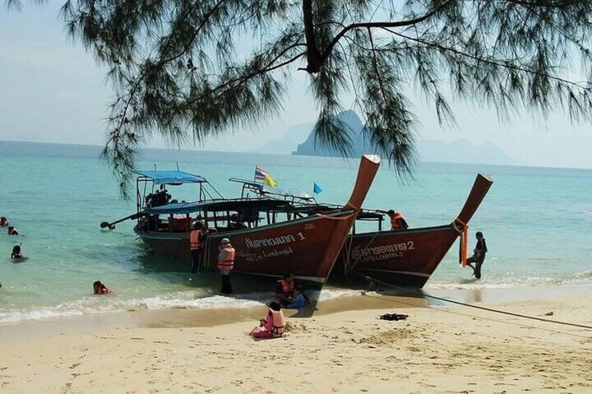 A beach with two large boats, people swimming, and a person sitting on the sand. 3