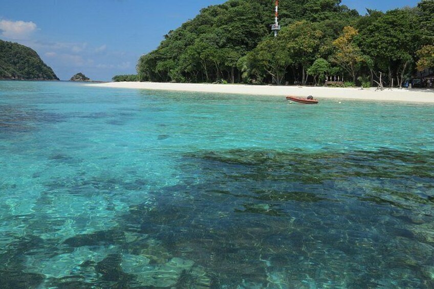 A clear turquoise sea, a small boat, and a white sandy beach with dense green foliage in the background. 3