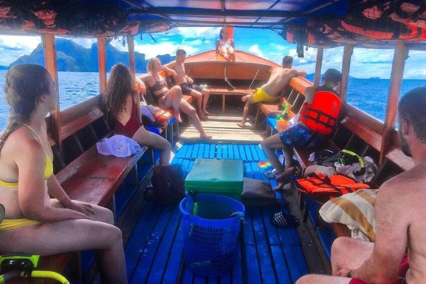 Een boot met mensen die op bankjes zitten, een persoon staat vooraan en een blauwe mat op het dek. 1