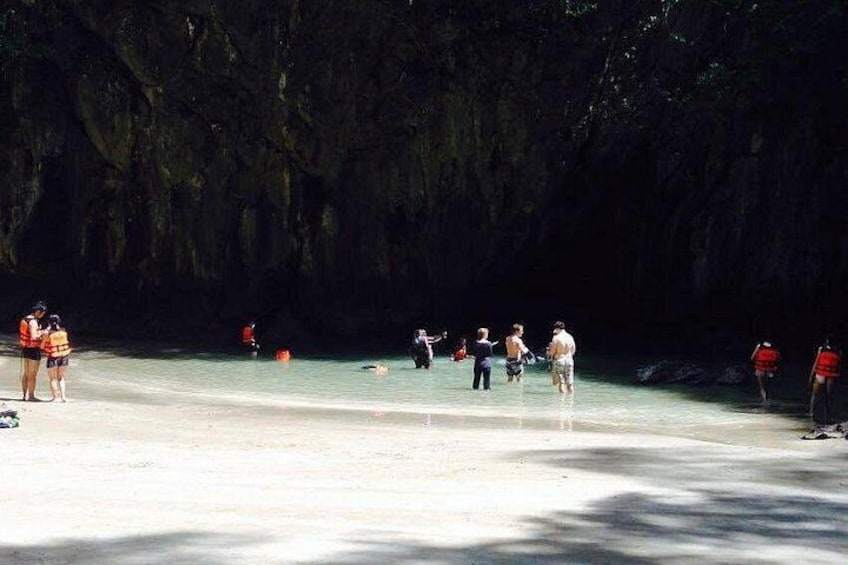 A beach with people standing and walking, surrounded by a rocky cliff. 3
