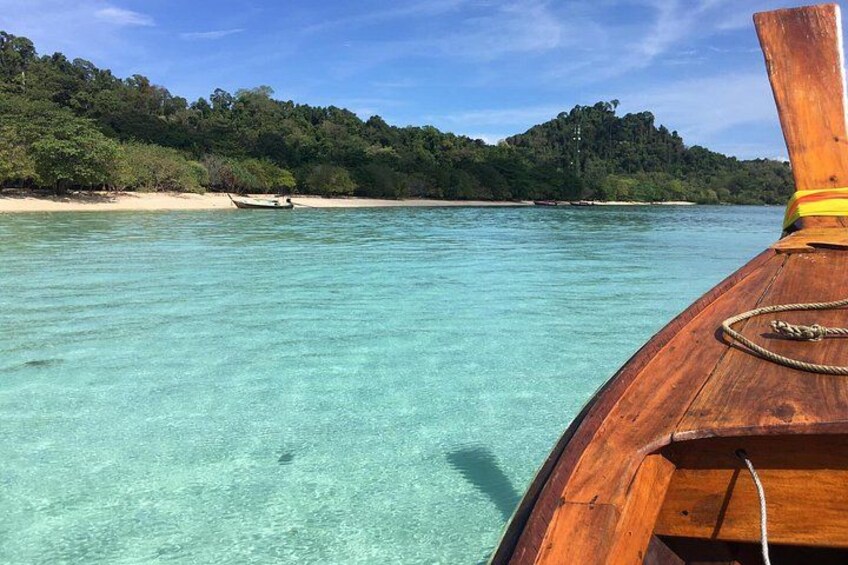Een houten boot op helder turquoise water, met een zandstrand en een dicht, groen bos op de achtergrond. 3