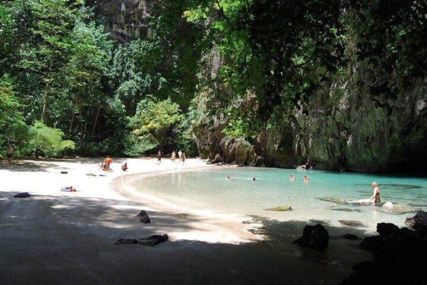 A beach with clear turquoise water, surrounded by lush greenery and rocky cliffs. 4