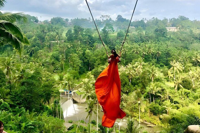 Eine Person, die an Seilen in einer üppigen, grünen Landschaft mit dichter Vegetation und blauem Himmel hängt. 2