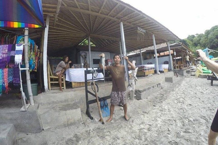A beachside market with a covered stall, colorful fabrics, and a person standing with a surfboard. 4