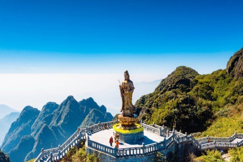 Una estatua en una montaña con una plataforma circular, rodeada por una barandilla de piedra y un cielo despejado. 2