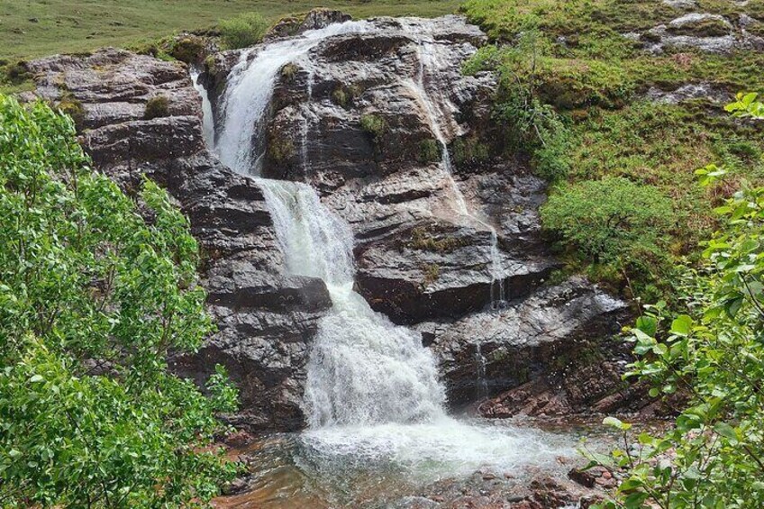 Ein Wasserfall stürzt über felsiges Gelände, umgeben von viel Grün. 5