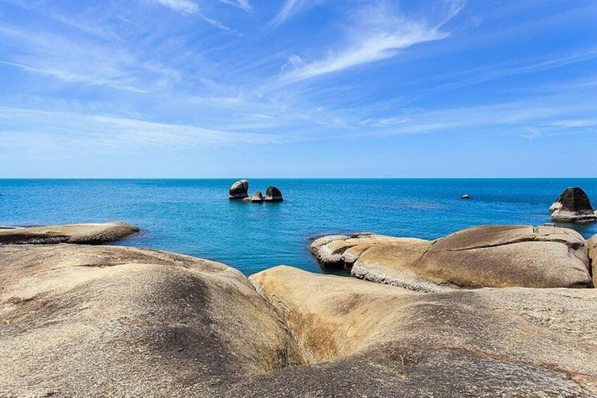 Un paysage côtier avec de gros rochers et une mer bleue et calme sous un ciel dégagé. 3