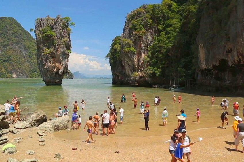 A beach with people sunbathing and swimming, surrounded by rocky cliffs and clear water. 2