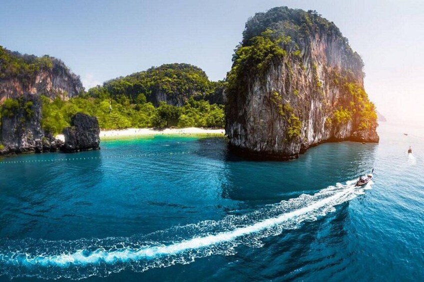 A boat on a turquoise sea with large limestone cliffs and a beach in the background. 3
