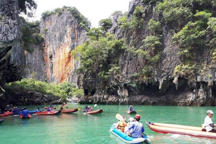 A group of people paddling in canoes on a calm river surrounded by rocky cliffs and lush greenery. 3