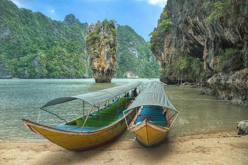 Two boats on a sandy shore with a large rock formation in the water. 2