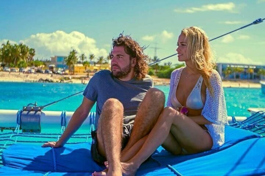 Two people sitting on a blue mat by a pool with a clear sky and palm trees in the background. 4