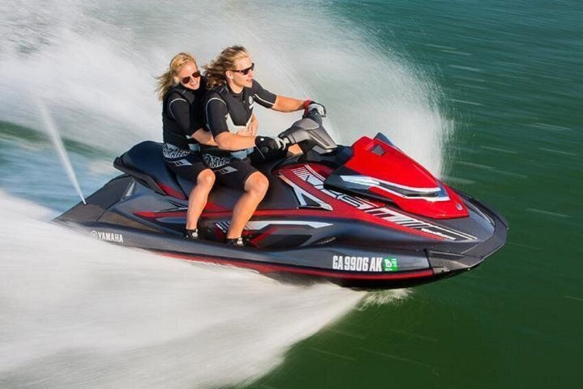Two people on a red and black Yamaha jet ski moving through water. 2