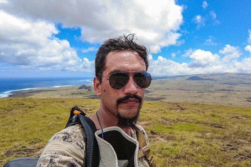 Une personne porte un sac à dos dans un champ herbeux, avec une vue sur l’océan et les nuages dans le ciel. 3