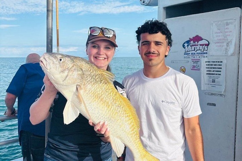 Two people holding a large fish on a boat with a sign for Murphy's Deep Sea Fishing. 1