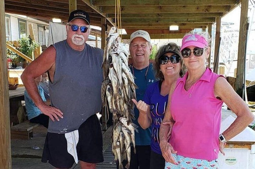 Four people standing in a covered area with a wooden structure, holding fish. 3