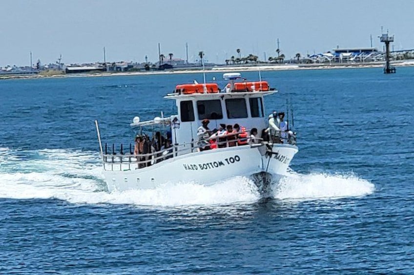 A white boat with 'NADO BOTTING 100' written on the side, moving on the water with passengers. 2