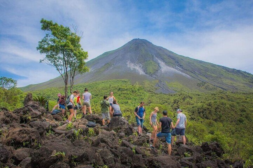 Een groep mensen wandelt over een vulkanisch landschap, met een berg op de achtergrond. 1
