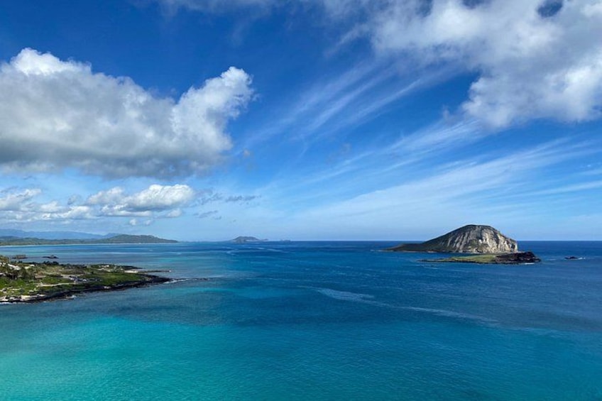 Un paisaje costero con aguas azules cristalinas, una pequeña isla y montañas distantes bajo un cielo parcialmente nublado. 5