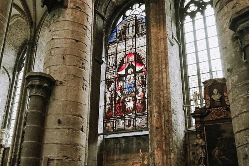Een glas-in-loodraam met religieuze afbeeldingen, stenen zuilen en een groot rondboogvenster. 2
