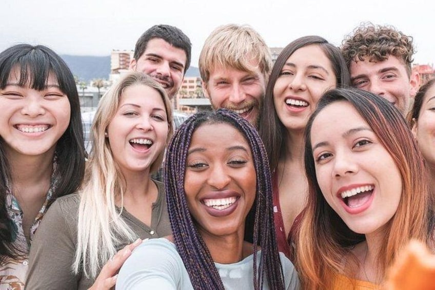 A group of people outdoors, possibly on a rooftop, with buildings and a clear sky in the background. 1