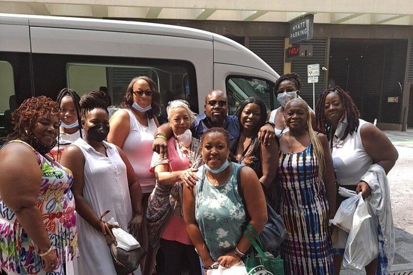 A group of people posing in front of a white van with a sign that reads 'HYATT PARKING' in the background. 4