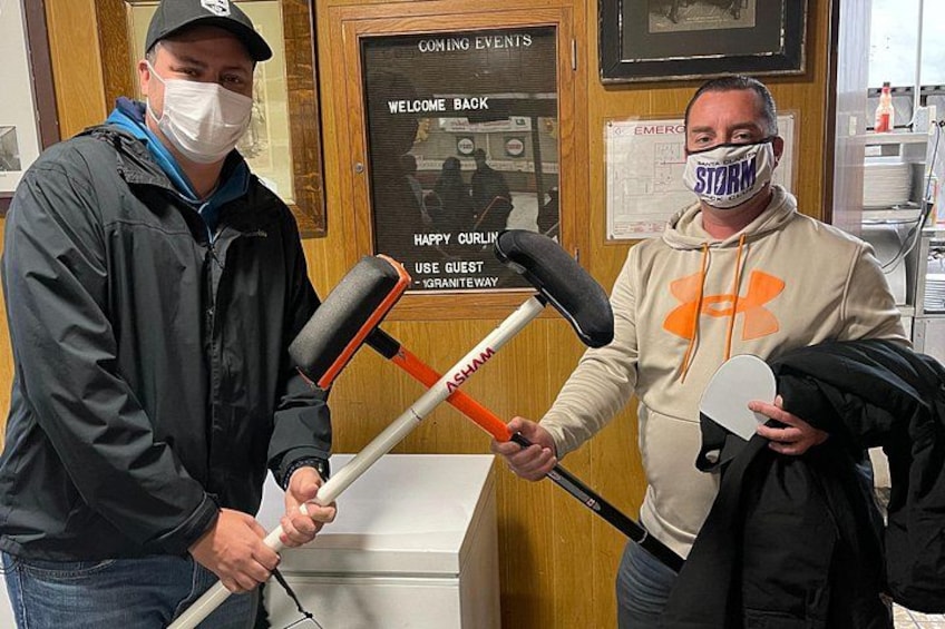 Two people holding bat and ball, standing in front of a wooden counter with a sign. 4