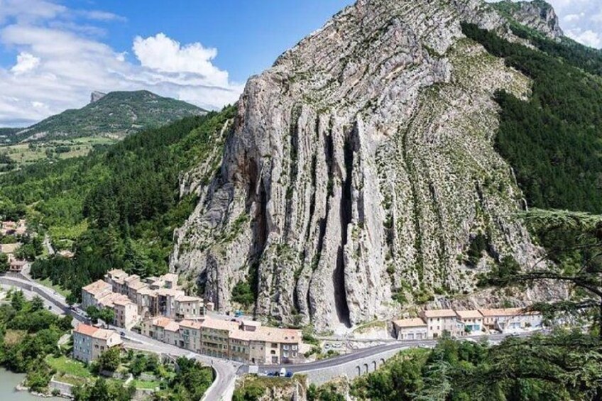 A mountainous landscape with a prominent rock formation, a winding road, and a small village with buildings. 2