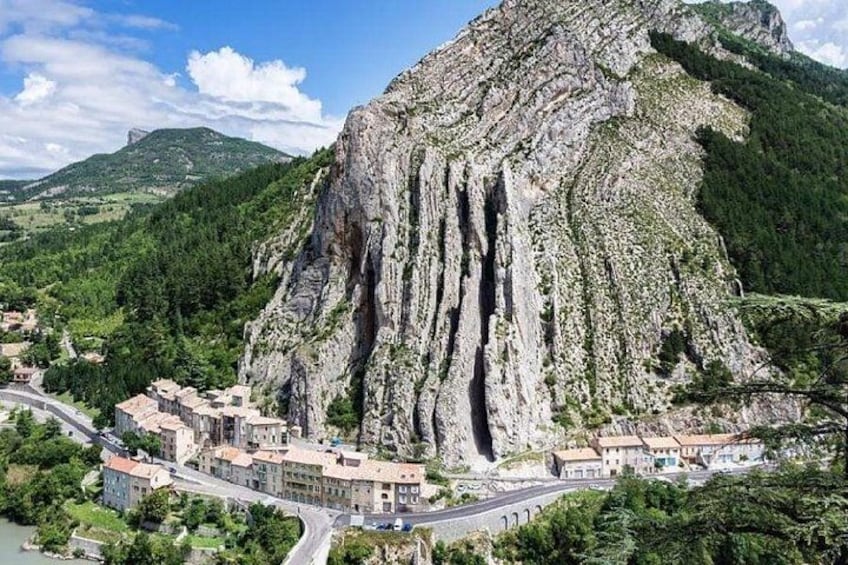 A mountainous landscape with a prominent rock formation, a village with buildings, and a winding road. 5