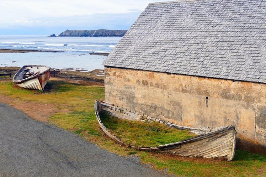 A coastal building with a stone exterior and a sloped roof, two boats on the grass, and the ocean in the background. 4