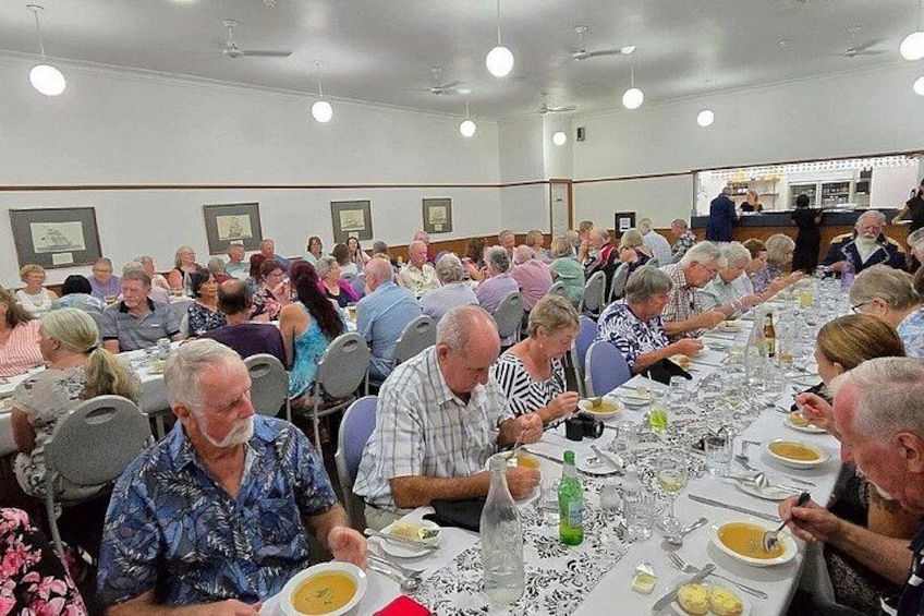 A large indoor gathering with people seated at tables, engaged in conversation and dining. 2