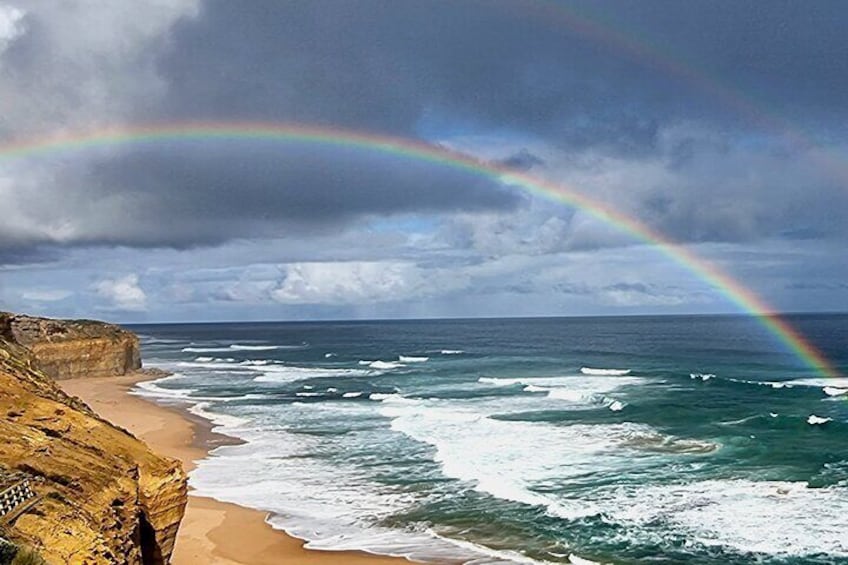 A beach with waves, a rainbow, and a rocky cliff. 3
