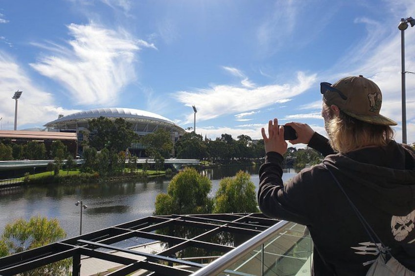 Iemand maakt een foto van een stadion, met een rivier op de voorgrond. 4