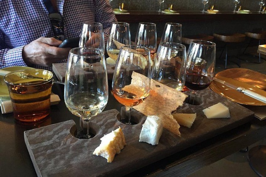 A bar setting with glasses of wine, a cheese board, and a person holding a phone. 1
