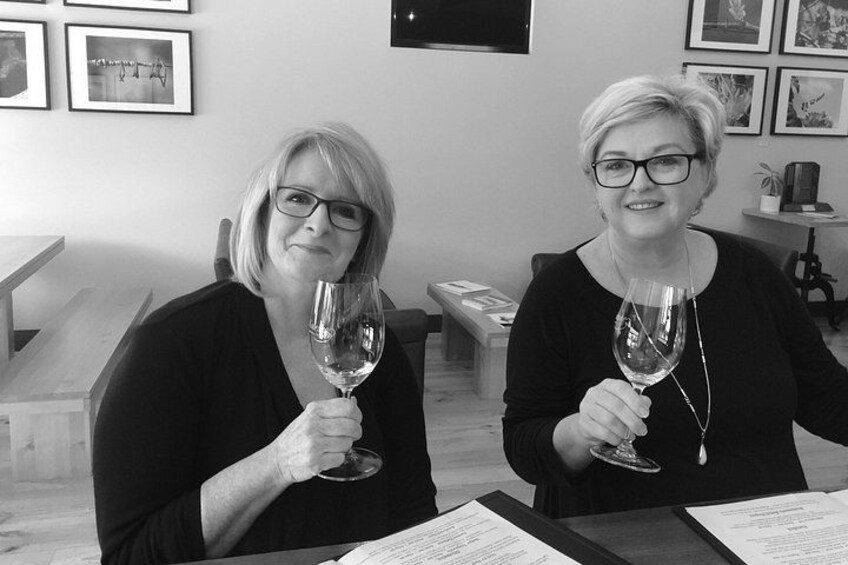 Two people holding wine glasses in a room with framed pictures on the wall. 2